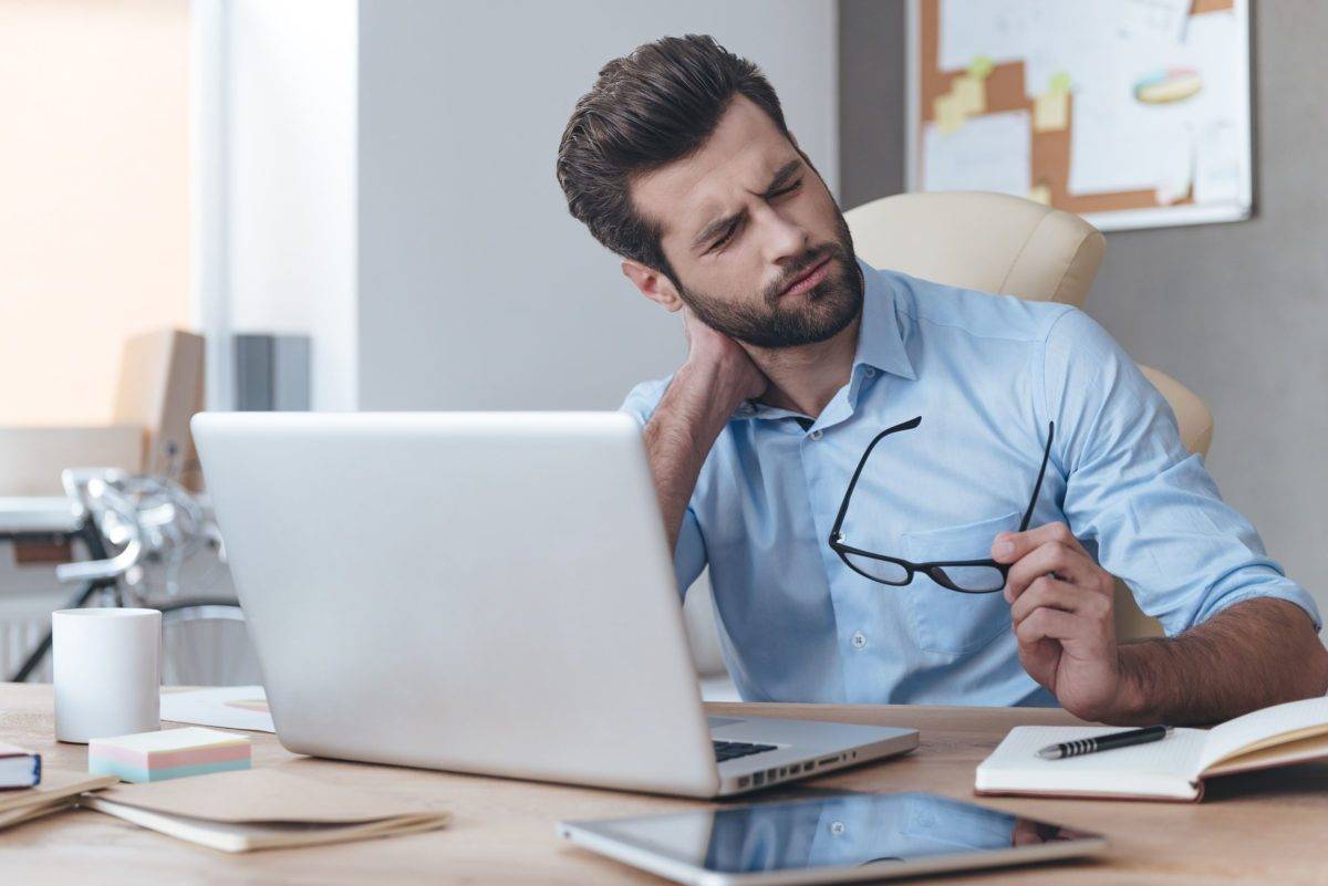 Feeling exhausted. Frustrated young handsome man looking exhausted while sitting at his working place and carrying his glasses in hand