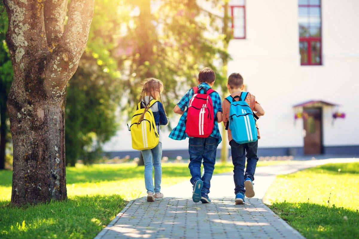 children with rucksacks standing in the park near school