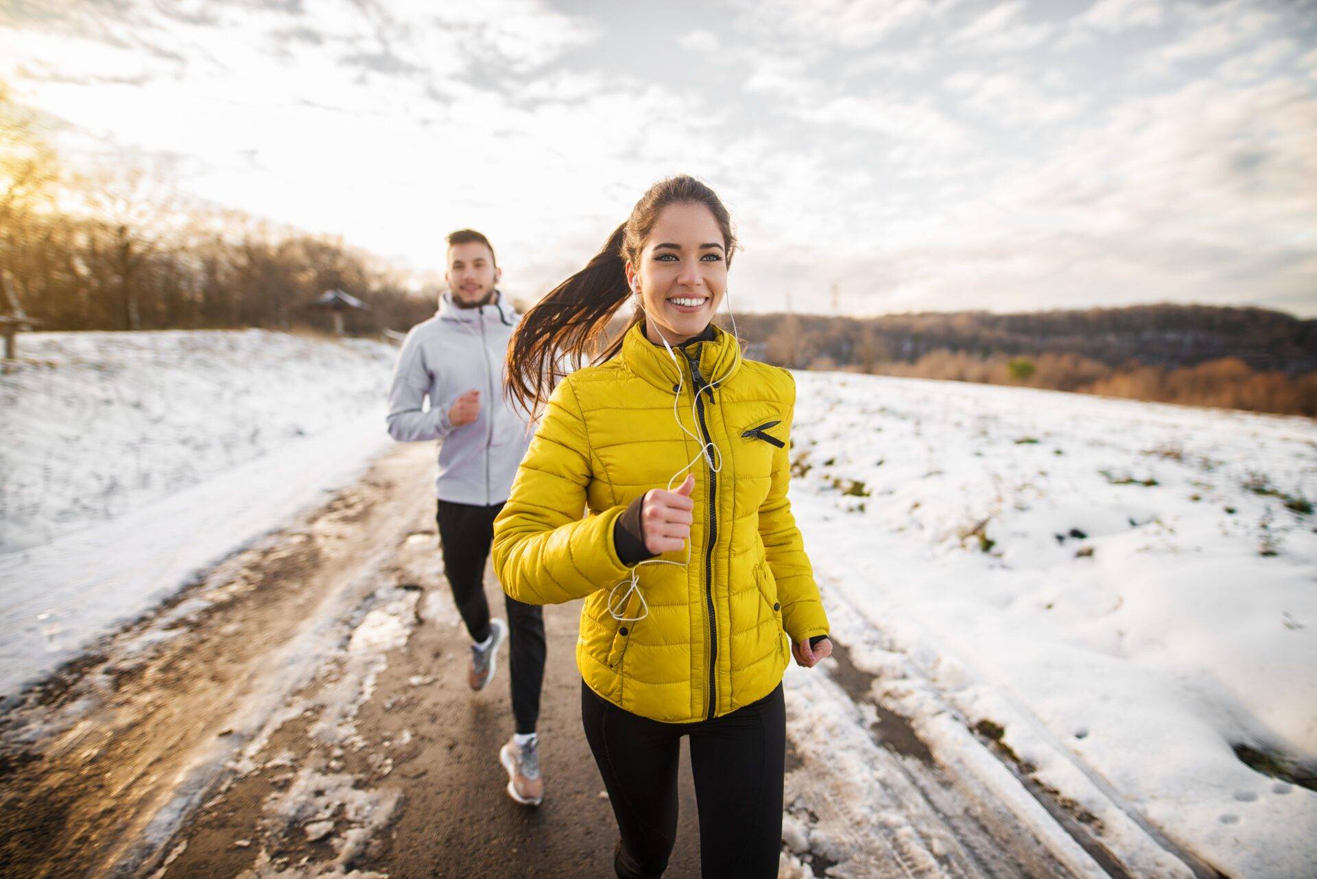 Beautiful happy active runner girl jogging with her personal handsome trainer on a snowy road in nature.