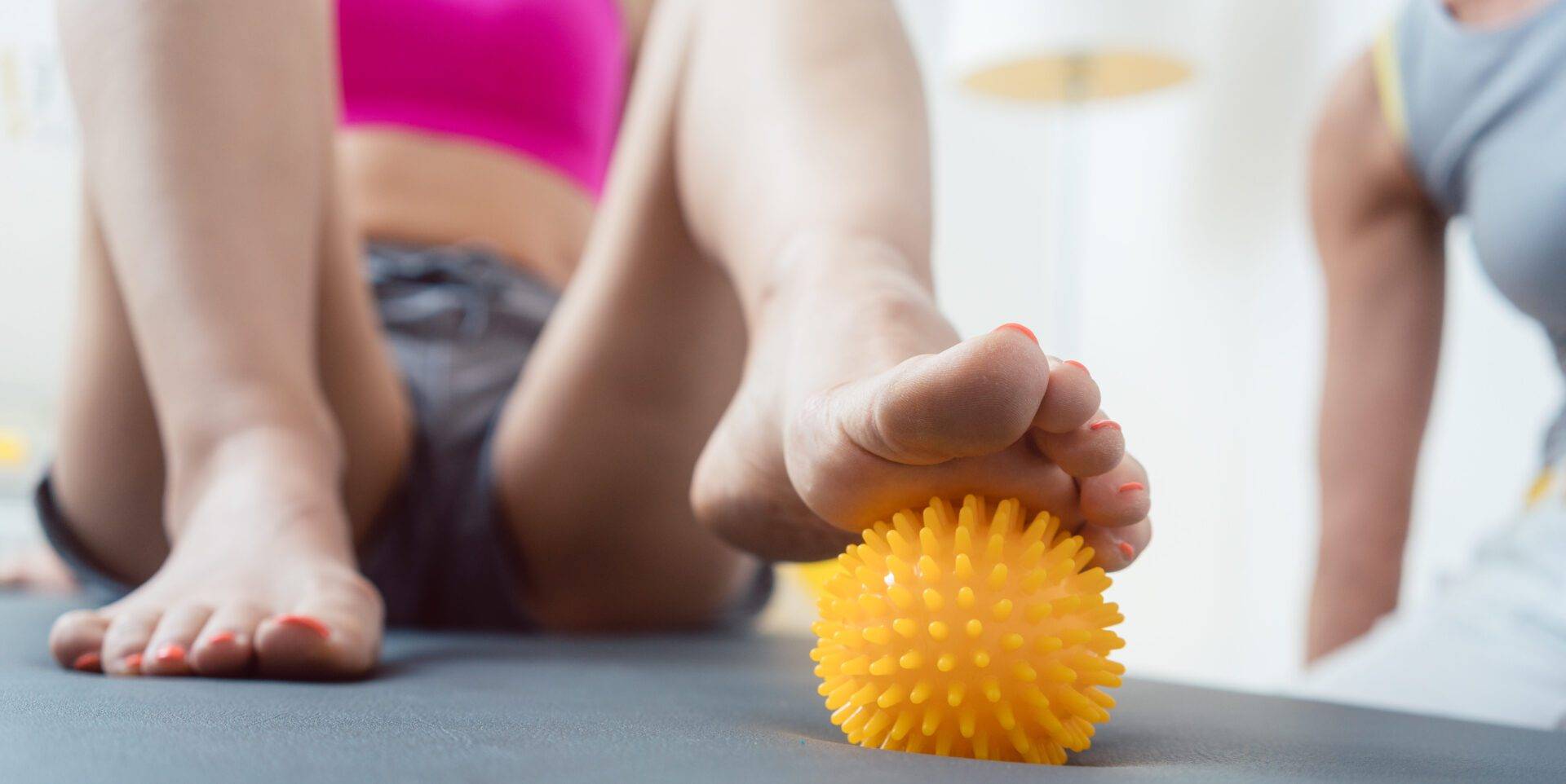 Woman rolling spiked ball under her feet in physical therapy